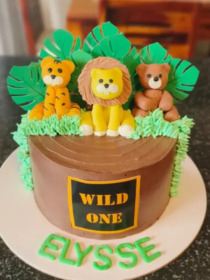 A "Wild One" first birthday cake with a chocolate log effect, topped with adorable fondant animals like a tiger, lion, and bear.