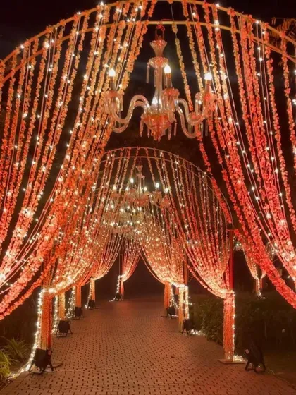 A warm and inviting entrance for an evening function, with arches wrapped in orange floral strings and fairy lights.