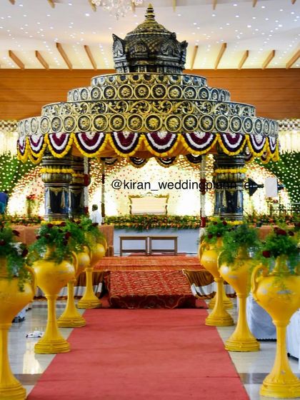 The path leading to a beautiful, ornate wedding mandap. The structure is decorated with traditional flower patterns and flanked by decorative yellow urns.