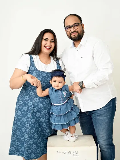 A joyful family of three. The parents hold their daughter's hands as she proudly stands, a perfect capture of a 7-month sitter milestone.