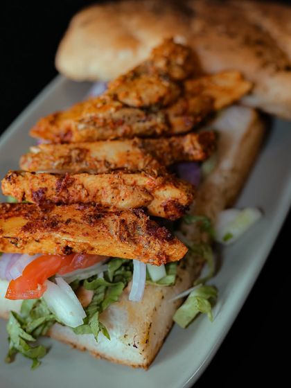 An open-faced view of the Chicken Tikka Panini, showing off the layers of seasoned chicken strips on a bed of fresh lettuce, onion, and tomato.