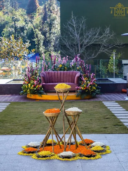 A beautiful Haldi setup with a focus on natural elements and vibrant colors. Baskets of fresh flower petals are arranged in a floral rangoli, creating a stunning and interactive centerpiece for the ceremony.