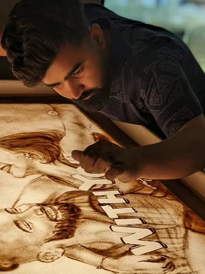 Using a fine tool to add details to the 'With You' sand art portrait.