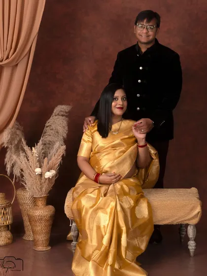 A regal seated portrait of the couple. The golden saree drapes beautifully, creating a look of timeless sophistication.
