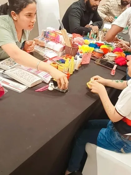 An instructor helping a child with their project at a busy craft table during a Barbie-themed birthday party.
