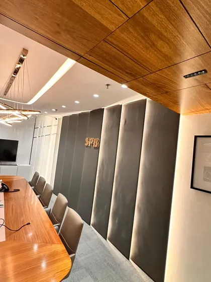 This shot highlights the material palette of the boardroom. The contrast between the warm wood ceiling panels, the soft grey acoustic wall, and the sleek white cabinetry creates a balanced and professional atmosphere.