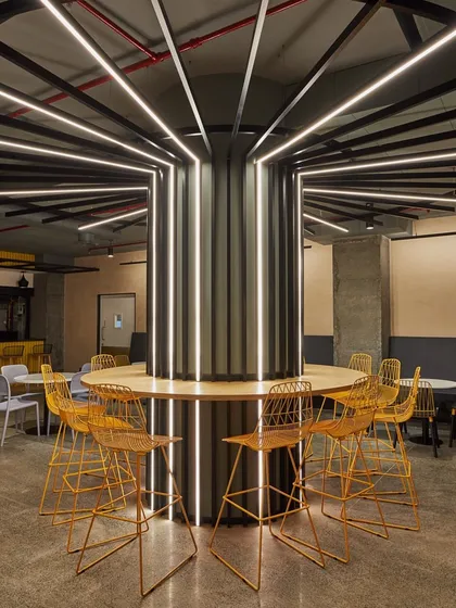 A striking seating area in a cafeteria, where the central column is wrapped in vertical light strips. The bright yellow chairs provide a strong visual accent.