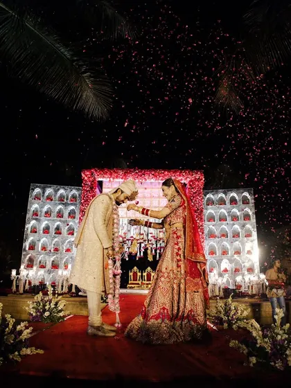 A beautiful varmala moment, with the couple framed by a stunning red and white floral arch and a backdrop of elegant niches.