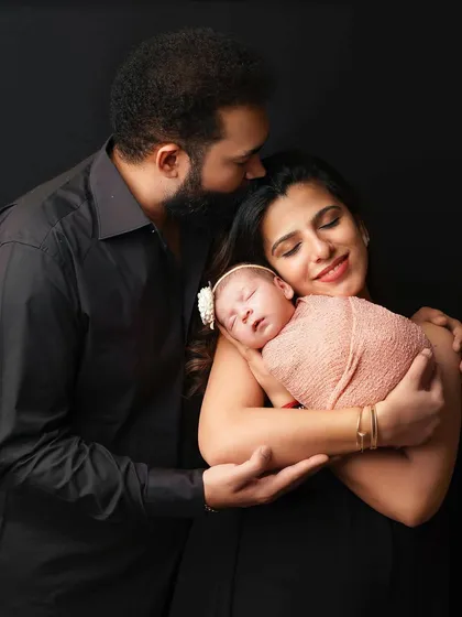 A mother and father embrace, holding their newborn baby safely between them. This pose is a beautiful symbol of family unity and love.