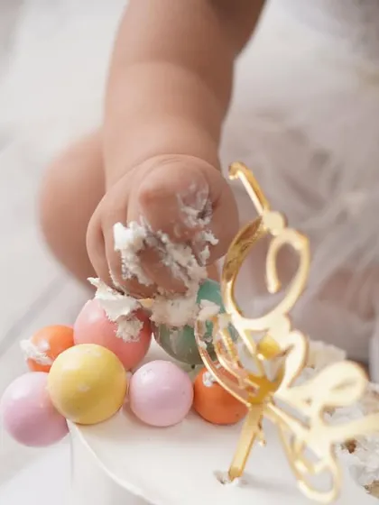 A macro shot of a baby's hand digging into a colorful birthday cake, capturing the messy fun of a cake smash.