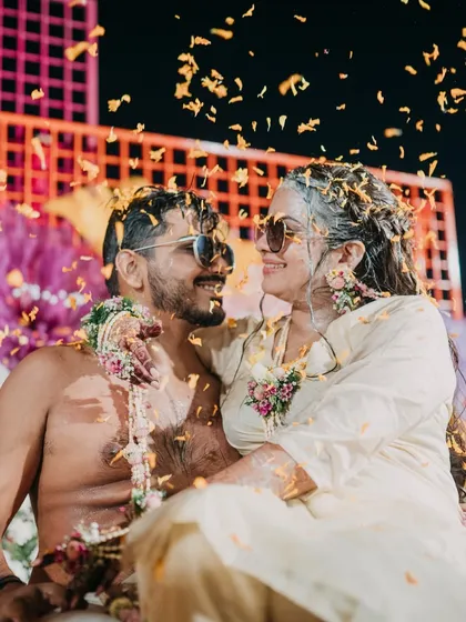 A cool and candid moment from the Haldi function. The couple, covered in turmeric and flowers, shares a sweet look, showcasing their fun-loving bond.