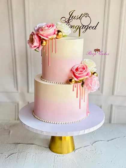 A beautiful two-tier engagement cake with a soft pink ombre drip effect. The design is finished with fresh roses and elegant pearl details, creating a look that is both modern and romantic.
