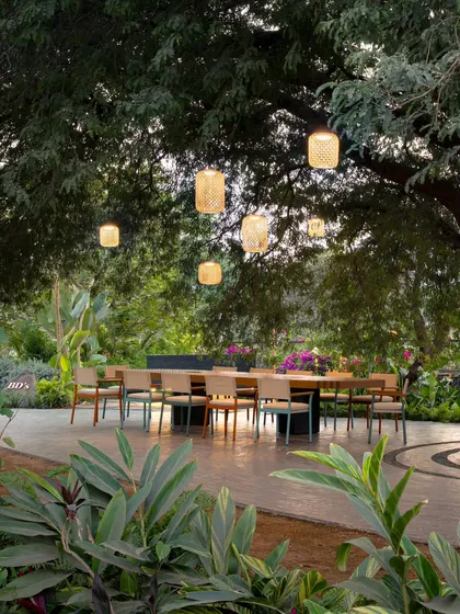 For this outdoor gathering space, we designed a series of custom woven pendant lights. They hang like lanterns from a large tamarind tree, creating a magical and intimate dining experience under the open sky.
