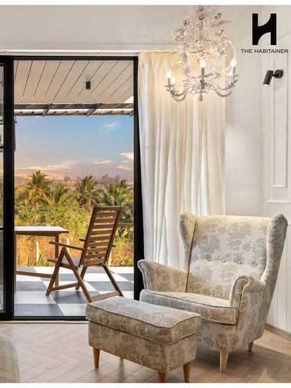 This cozy reading corner in the French-themed villa features an elegant wingback chair and ottoman. The crystal chandelier adds a touch of classic charm, while the large glass door offers a beautiful view.