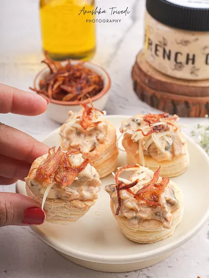 Creamy French onion dip served in flaky vol-au-vent pastries. The hand holding one up close highlights the texture and makes it look like the perfect party bite.