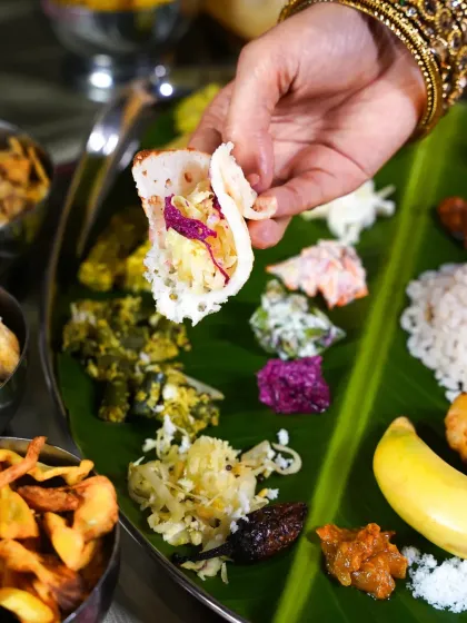 A hand enjoying a bite of the Onam Sadhya with an appam. This shot captures the communal and tactile experience of eating a traditional Indian feast.