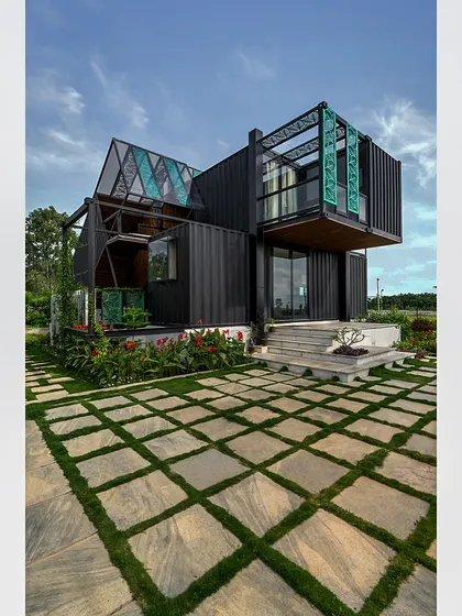 This angle of the container home highlights its cantilevered upper level, a feat of modern engineering. The image showcases the dynamic, multi-layered facade and its relationship with the surrounding garden.