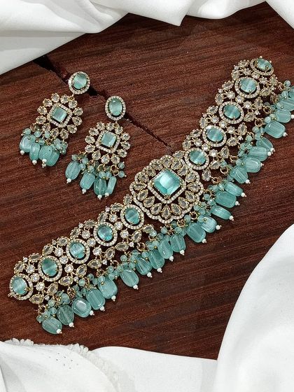 A versatile choker set available in multiple colors including white pearl, ruby, emerald, and pastel pink. The design features a central square motif with hanging beads, making it a popular choice for various festive occasions.