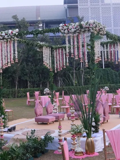 A closer look at the pink and green mandap, highlighting the intricate hanging floral decorations made from rajnigandha (tuberose) and pink flowers, along with traditional temple bells.