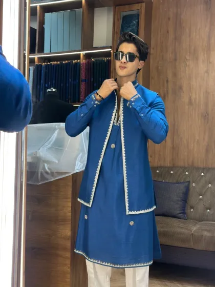 A client admiring his reflection in a custom royal blue layered kurta. The perfect fit and the fine details on the jacket make this a standout piece for any wedding.
