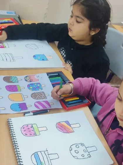 Two students working on their ice cream drawings. It's fun to see how they each choose different colors and patterns for their popsicles.