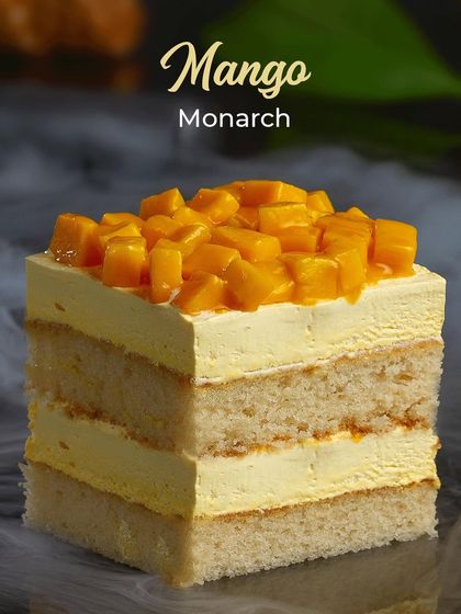 The Mango Monarch is a layered pastry celebrating the king of fruits. It features soft vanilla sponge alternating with creamy mango mousse and is generously topped with fresh mango chunks.