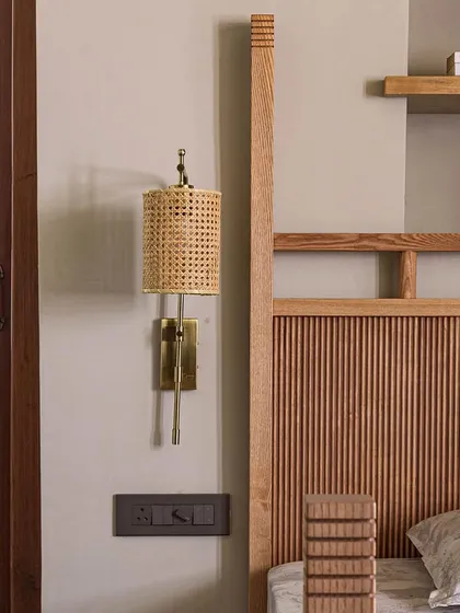 A detail of the custom bed in Apartment 5026, highlighting the woven cane wall sconce and intricate woodwork. This focus on craftsmanship and natural materials is central to our design philosophy, adding warmth and texture to the space.