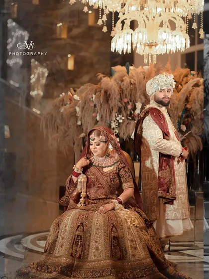 A regal and stylish wedding portrait of the couple. The bride is seated majestically while the groom stands by her side, creating a powerful and elegant image.