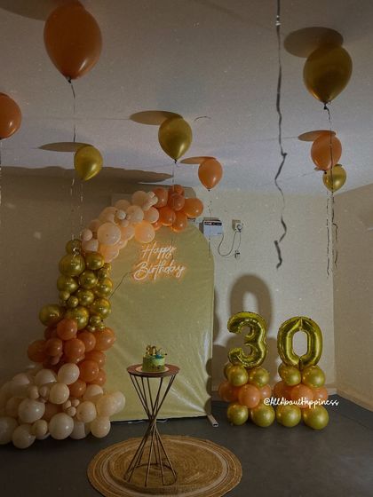 A cozy and stylish 30th birthday setup in a home, featuring a balloon arch, a neon sign, and foil number balloons.