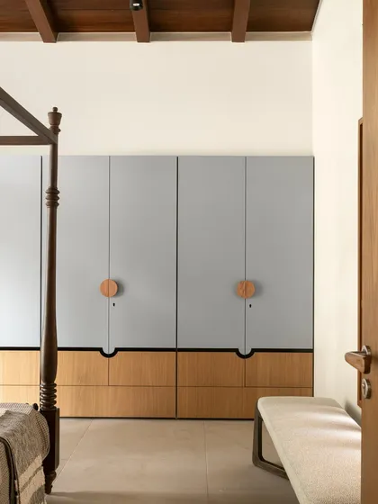 These bespoke wardrobes blend a soft, powdery grey with warm oak. The oversized circular wooden pulls act as modern Kolam-inspired strokes, adding a graphic and tactile detail to the minimalist design.