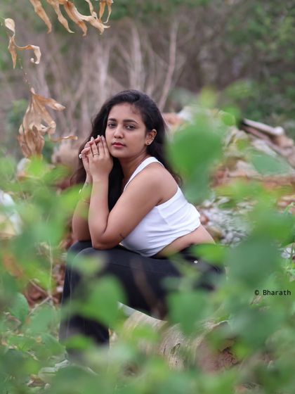 A creative outdoor shot, using blurred foreground leaves to frame the subject and create a sense of peeking into a private moment.