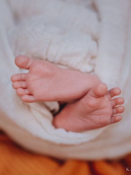 Another adorable shot of tiny feet, this time peeking out from a white swaddle against a warm orange blanket. The contrast in colors makes the details pop.