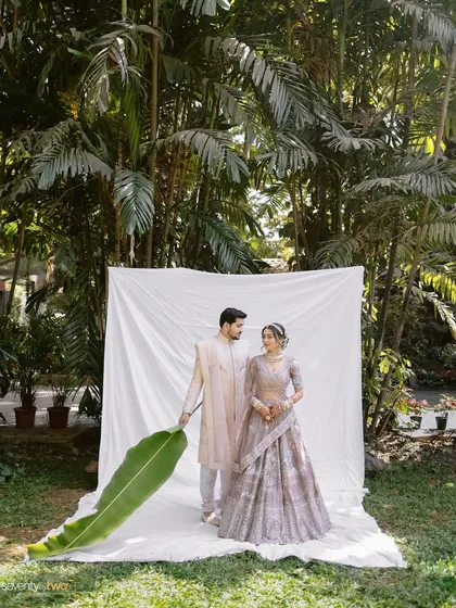 A wide shot of our minimal outdoor studio setup, with the couple framed by a white backdrop and a large banana leaf, showing how we create art amidst nature.