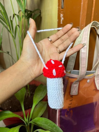 A hand holding the red and white crochet mushroom lip balm holder.