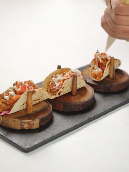 A chef adds the finishing touch of lime cream to our phulka tacos. This small detail balances the spiced jackfruit and adds a cooling, creamy element.