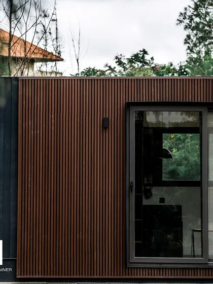 The exterior of a 20ft container home, featuring a combination of dark corrugated steel and warm, fluted WPC cladding. This shows how different materials can be used to add texture and style to a small structure.