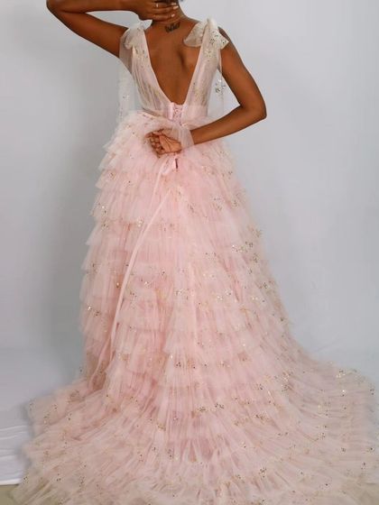 The back of this dreamy pink gown features a low V-back and delicate bow details on the shoulders, with a skirt made of soft, layered ruffles.