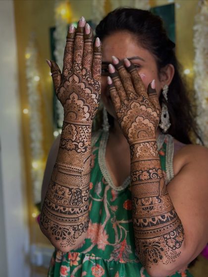 A happy bride peeking through her hands, covered in a dense and beautiful bridal design.