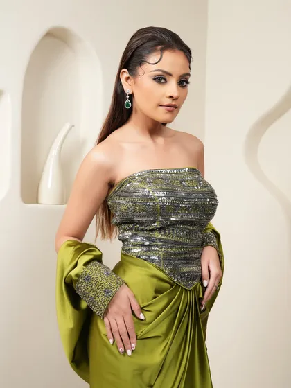 A crisp studio shot for an e-commerce fashion brand. The clean background and even lighting ensure the focus remains on the sequined corset top and olive green draped skirt.