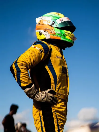 A driver in a yellow race suit, looking out over the track.