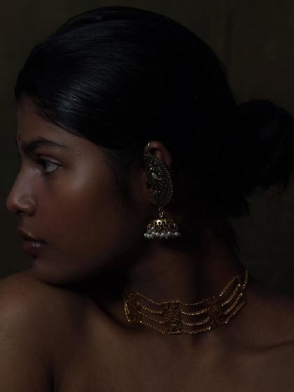 A serene profile shot from the "golden tones" series. The light beautifully catches the intricate details of the traditional jhumka earring and the delicate choker, creating a timeless and elegant portrait.