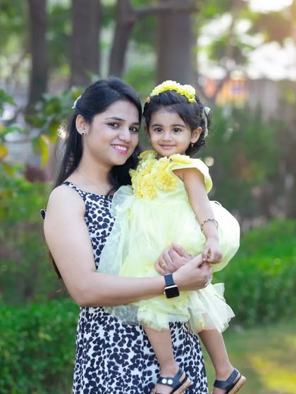 A mother holds her daughter, both dressed in cheerful yellow, sharing a beautiful smile for the camera. A perfect portrait of mother-daughter love in the golden light of the park.