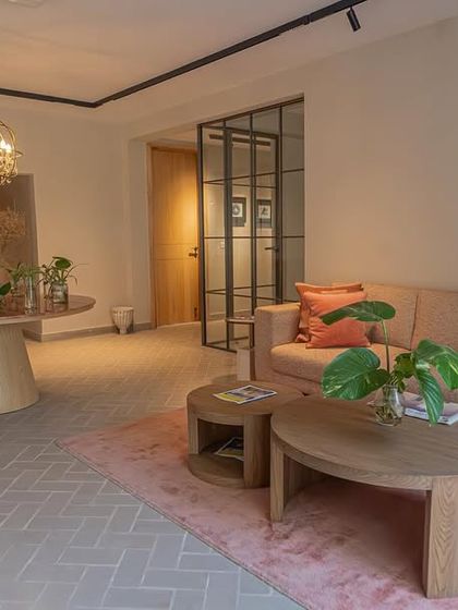 The waiting area of a modern office we designed, featuring our custom-made furniture. The space includes a comfortable sofa, nested wooden coffee tables, and a round pedestal table, all in soft, earthy tones.