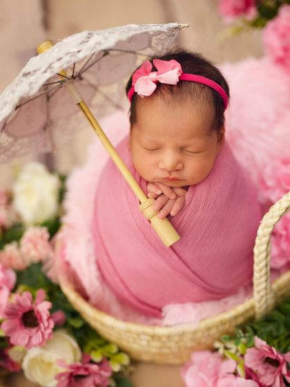 Pretty in pink. This newborn is swaddled in a soft pink wrap, holding a tiny lace parasol and surrounded by pink blossoms.
