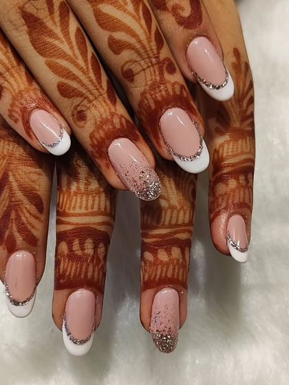 A classic bridal choice with a touch of sparkle. This look features a timeless French manicure on oval nails, elevated with a full glitter accent nail and a fine line of silver glitter along the tips for a sophisticated wedding style.