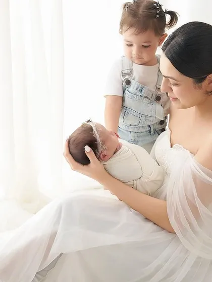 A beautiful moment as a mother introduces her newborn to their older sibling. This bright, all-white studio setting is perfect for capturing the start of a lifelong friendship.