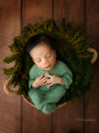 Three-week-old Abir resting in a mossy green basket. The overhead angle and cozy outfit create a portrait that is both adorable and artistic.