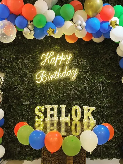 A colorful balloon arch against a green wall for an 8th birthday party, featuring a neon sign and marquee letters.
