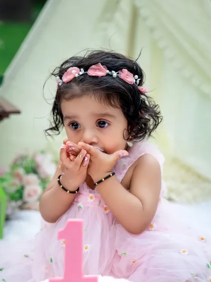 A close-up of the birthday girl enjoying her cake. Those sweet, frosting-covered fingers are a detail that perfectly captures the fun of a cake smash.