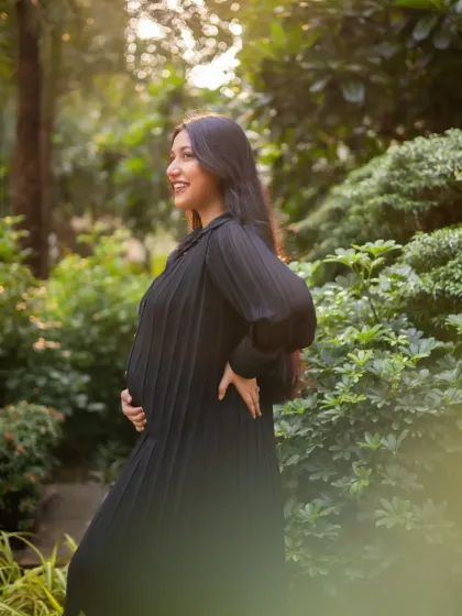The expecting mother is captured in beautiful side-profile light, smiling as she looks into the distance. This shot highlights her happy glow against a garden backdrop.